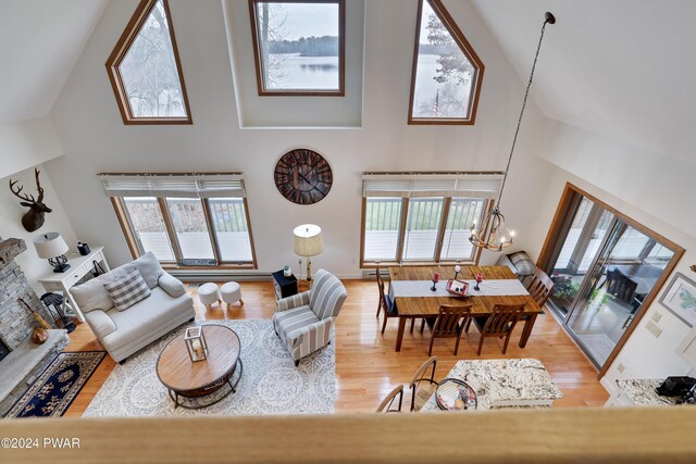 living room with a chandelier, wood-type flooring, high vaulted ceiling, and a stone fireplace