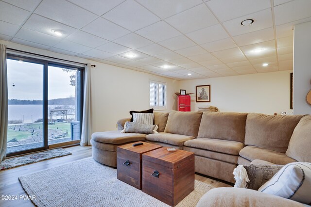 living room with a paneled ceiling, a water view, and light wood-type flooring