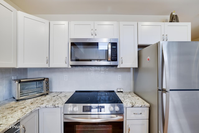 kitchen with white cabinets, appliances with stainless steel finishes, backsplash, and light stone counters