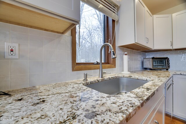 kitchen featuring light stone counters, white cabinetry, tasteful backsplash, and sink