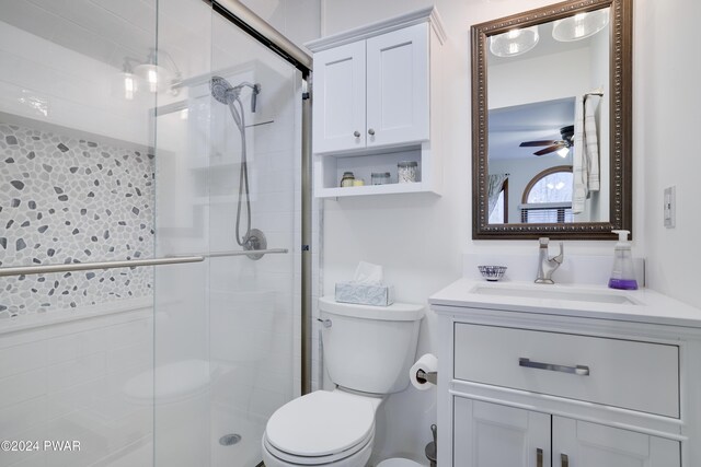 bathroom featuring ceiling fan, toilet, a shower with shower door, and vanity