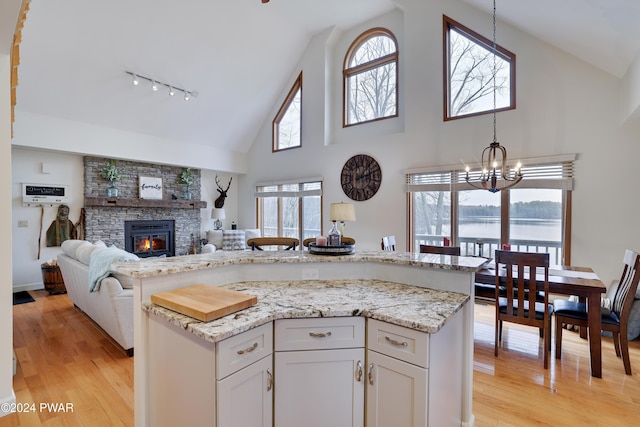 kitchen with white cabinets, a water view, light hardwood / wood-style flooring, light stone countertops, and a fireplace