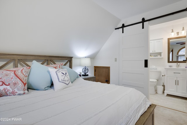 bedroom with connected bathroom, a barn door, and vaulted ceiling