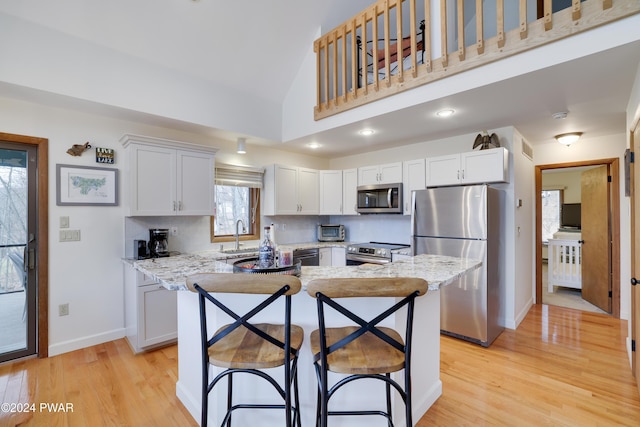 kitchen featuring a kitchen breakfast bar, light stone counters, stainless steel appliances, light hardwood / wood-style floors, and white cabinetry