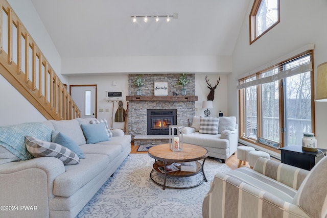 living room with high vaulted ceiling, a stone fireplace, a wealth of natural light, and track lighting