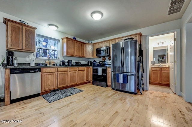 kitchen featuring brown cabinetry, visible vents, stainless steel appliances, and light wood-style floors