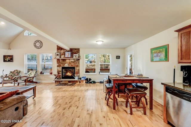 dining room with a stone fireplace, light wood-style flooring, baseboards, and vaulted ceiling