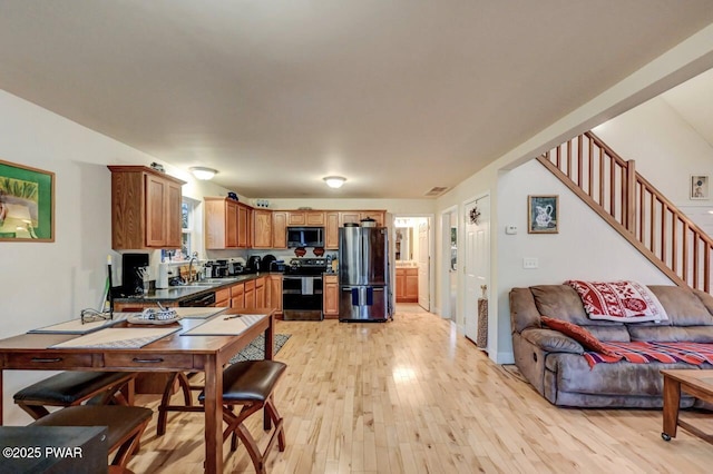 kitchen featuring a sink, dark countertops, open floor plan, stainless steel appliances, and light wood finished floors