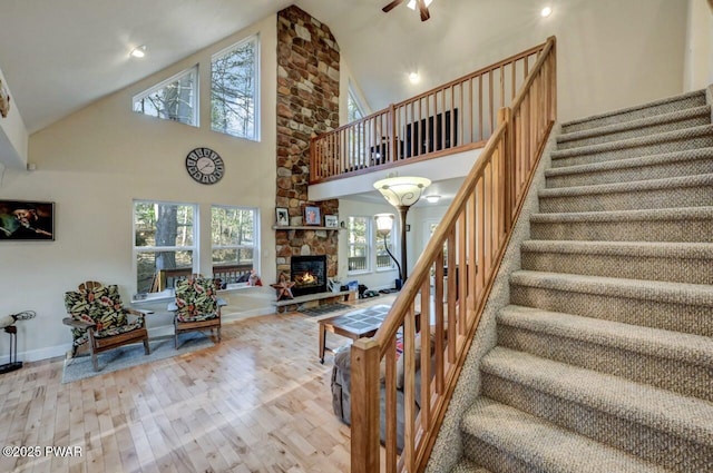 stairs with high vaulted ceiling, a ceiling fan, wood finished floors, a fireplace, and baseboards