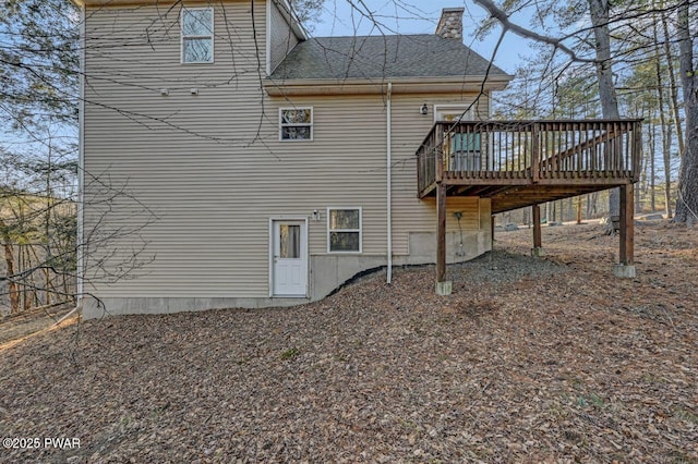 rear view of property featuring a deck, roof with shingles, and a chimney