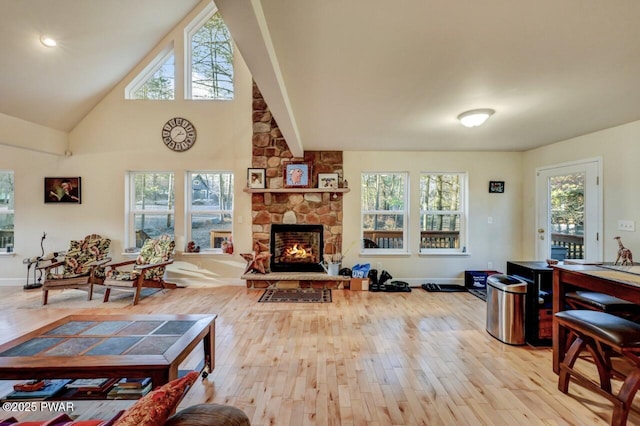 living room with light wood finished floors, a stone fireplace, high vaulted ceiling, and baseboards