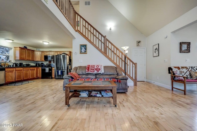 living room featuring stairway, a towering ceiling, baseboards, and light wood finished floors