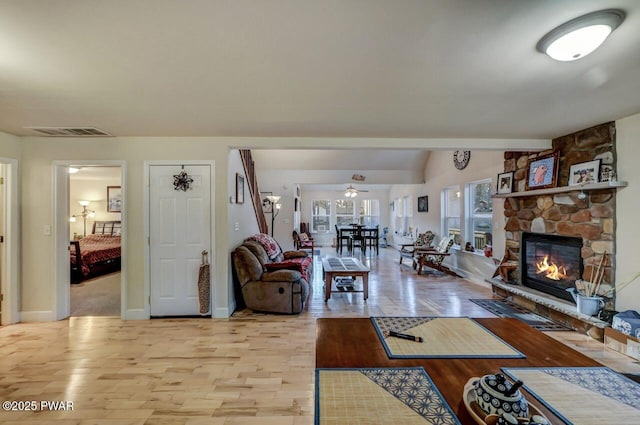 living area featuring visible vents, a ceiling fan, a stone fireplace, light wood finished floors, and vaulted ceiling