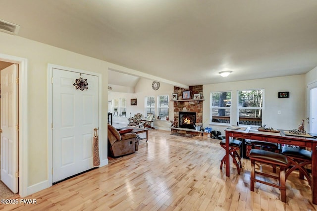 dining room featuring light wood finished floors, visible vents, baseboards, vaulted ceiling, and a stone fireplace