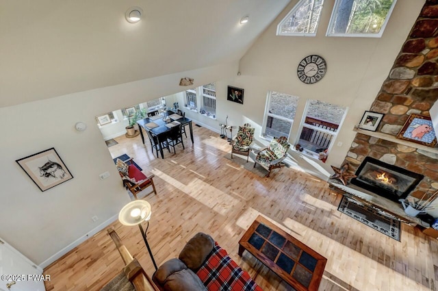 living area with wood finished floors, a fireplace, baseboards, and high vaulted ceiling