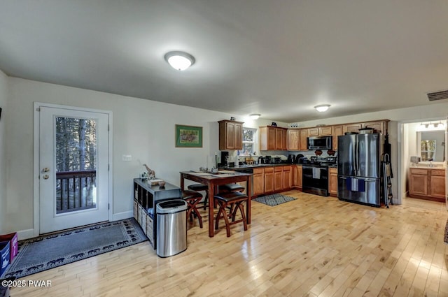 kitchen featuring stainless steel microwave, light wood-style floors, black range with electric cooktop, and freestanding refrigerator