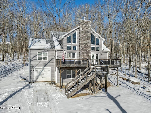 snow covered back of property with a garage and a deck