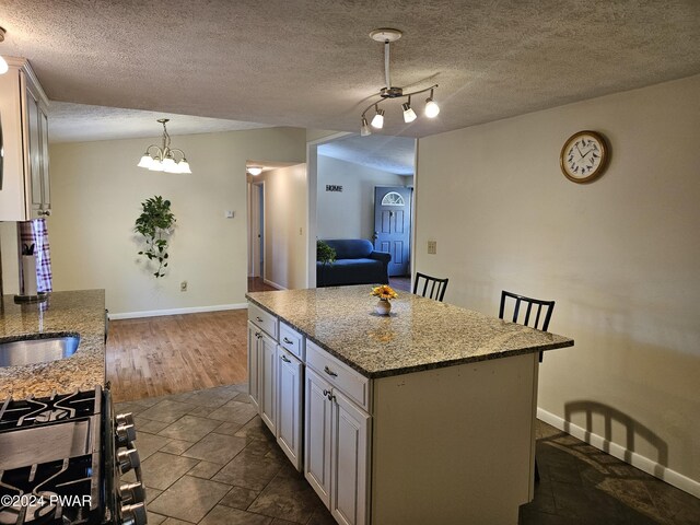 kitchen featuring light stone countertops, hanging light fixtures, a notable chandelier, a kitchen bar, and a kitchen island