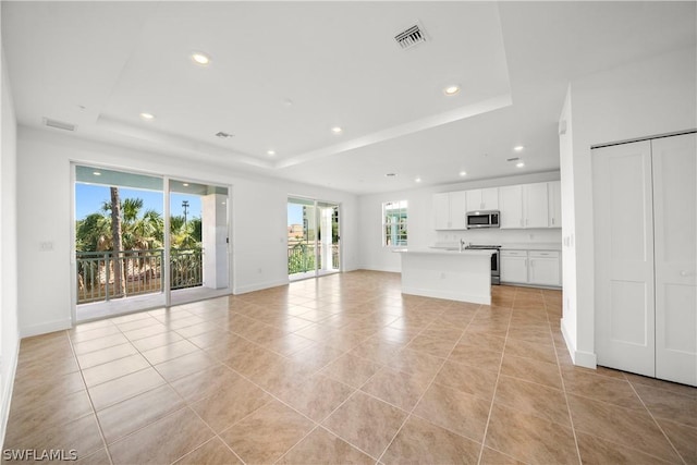 unfurnished living room featuring light tile patterned flooring and a tray ceiling