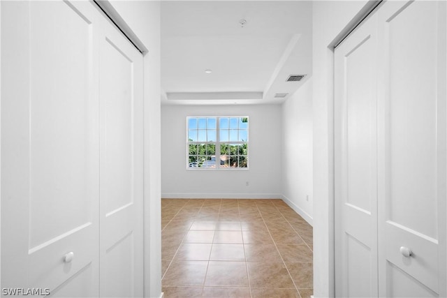 interior space featuring light tile patterned floors, visible vents, a raised ceiling, and baseboards