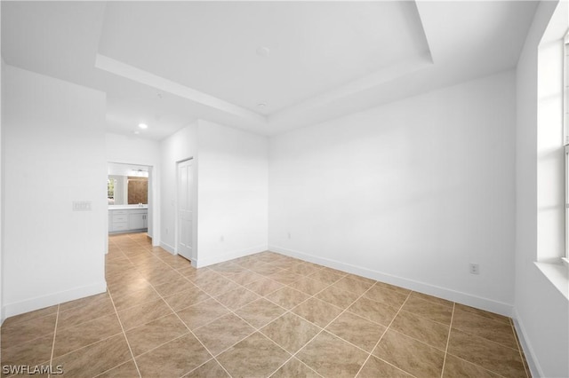 empty room featuring light tile patterned floors, a raised ceiling, and baseboards