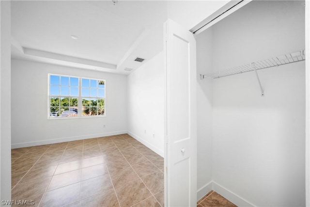 unfurnished bedroom with a tray ceiling, light tile patterned flooring, visible vents, and baseboards