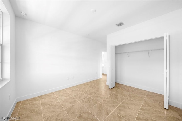 unfurnished bedroom featuring tile patterned floors, visible vents, baseboards, and a closet