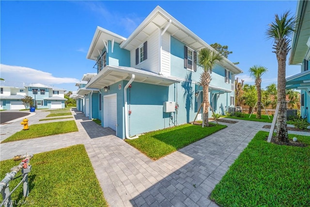 view of front of home featuring a front lawn, a residential view, stucco siding, decorative driveway, and a garage