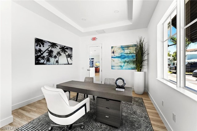 home office featuring a raised ceiling, light wood-style floors, and baseboards