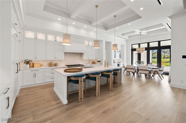 kitchen with tasteful backsplash, an island with sink, light wood-style flooring, beamed ceiling, and light countertops