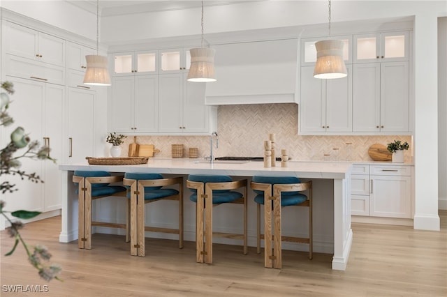 kitchen with a center island with sink, light wood finished floors, glass insert cabinets, white cabinetry, and a kitchen breakfast bar