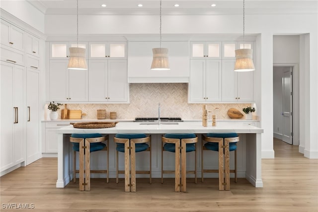 kitchen featuring a center island with sink, light countertops, a kitchen bar, white cabinetry, and a sink