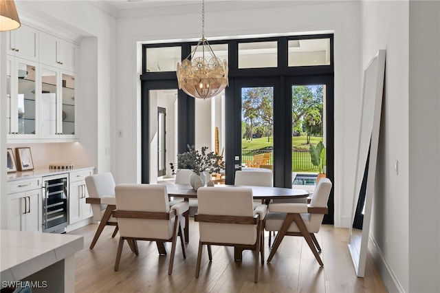 dining room featuring a notable chandelier, beverage cooler, a dry bar, baseboards, and light wood finished floors