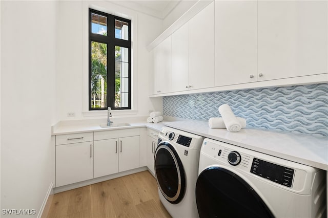 washroom featuring light wood-style flooring, washing machine and clothes dryer, a sink, and cabinet space