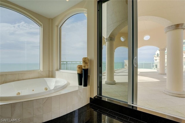 bathroom featuring a water view, granite finish floor, a tub with jets, and decorative columns