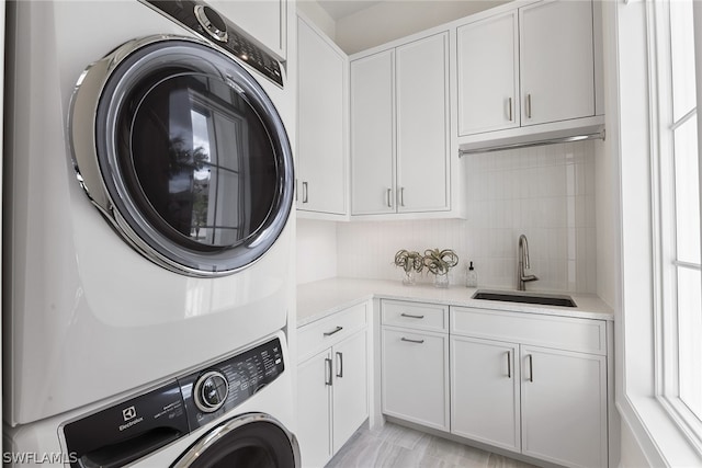 laundry room featuring cabinets, stacked washer / dryer, and sink