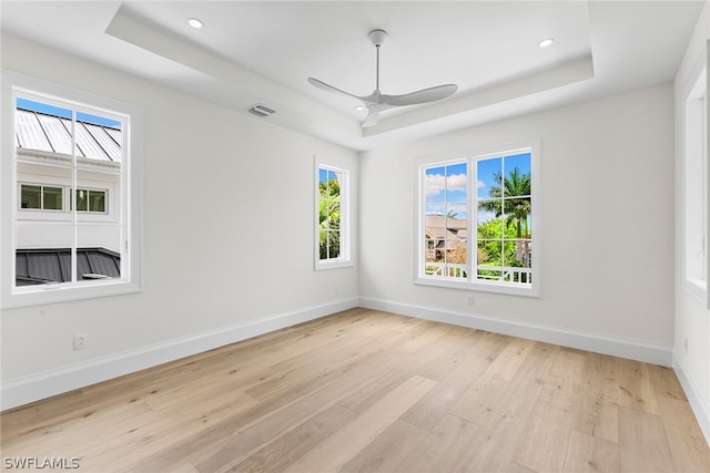 empty room with ceiling fan, a tray ceiling, and light wood-type flooring