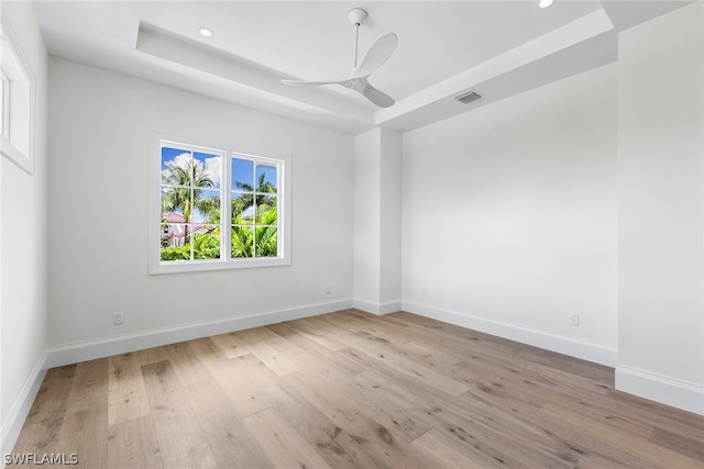 unfurnished room with a raised ceiling, ceiling fan, and light hardwood / wood-style floors