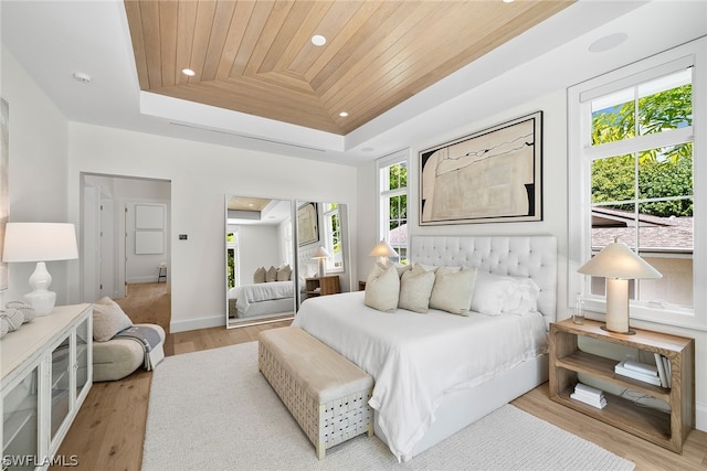 bedroom featuring wooden ceiling, light hardwood / wood-style flooring, multiple windows, and a tray ceiling