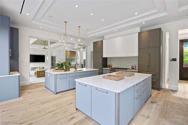 kitchen with light wood-type flooring, a center island with sink, and a tray ceiling