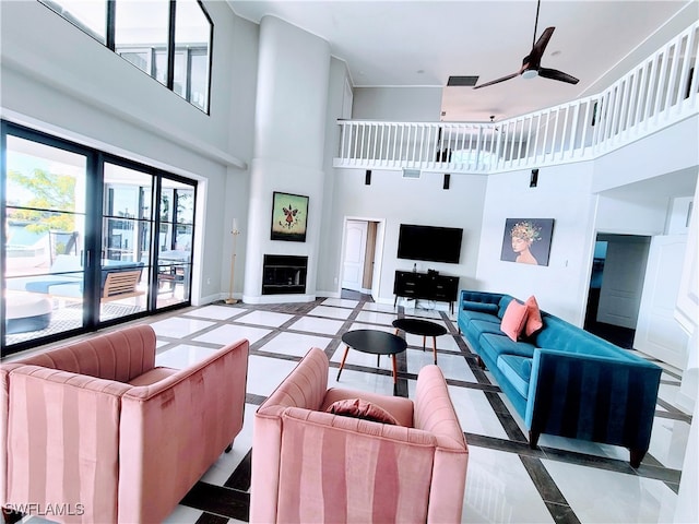 living room featuring a high ceiling, ceiling fan, and a large fireplace