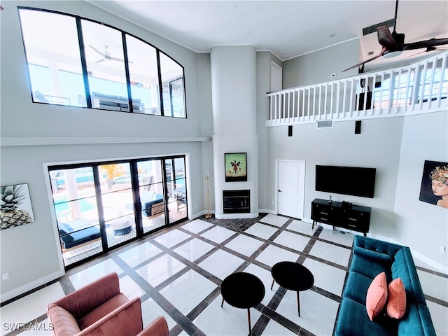 tiled living room with a towering ceiling, ceiling fan, and a fireplace