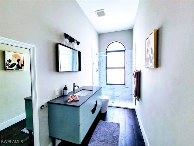 bathroom with toilet, vanity, hardwood / wood-style flooring, and a tile shower