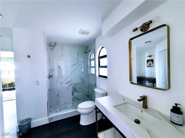 bathroom with toilet, hardwood / wood-style flooring, a tile shower, and a healthy amount of sunlight