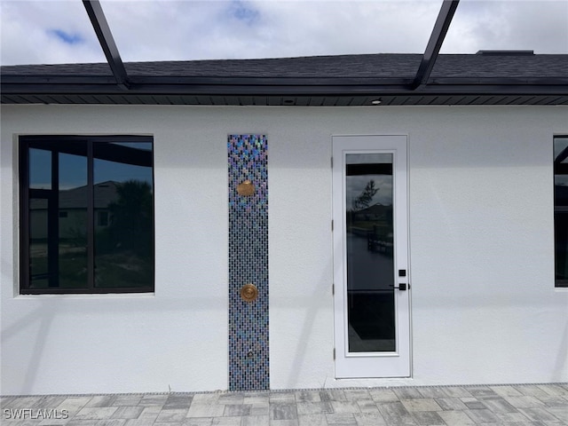 property entrance featuring stucco siding and a shingled roof