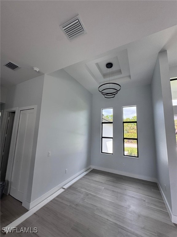 empty room featuring visible vents, baseboards, a tray ceiling, and wood finished floors