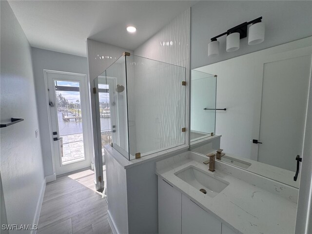 bathroom with a walk in shower, vanity, baseboards, and wood finished floors