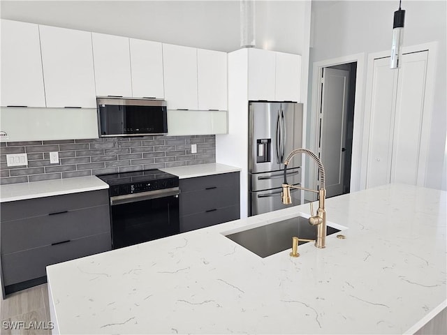 kitchen with backsplash, light stone countertops, gray cabinets, appliances with stainless steel finishes, and a sink