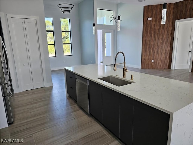 kitchen featuring a sink, dark cabinetry, freestanding refrigerator, dishwasher, and hanging light fixtures