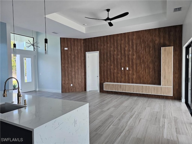 living area featuring wooden walls, visible vents, a tray ceiling, light wood-style flooring, and a ceiling fan